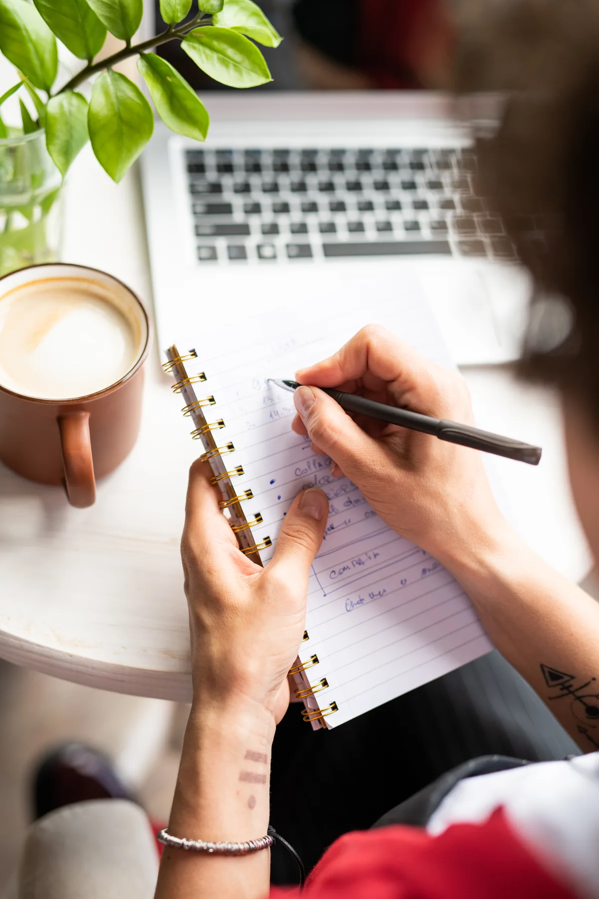 A small-business owner taking notes by a laptop and coffee