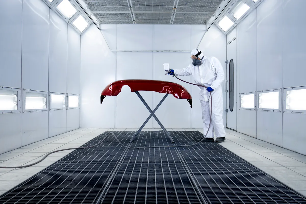 Technician painting a car in a body shop booth