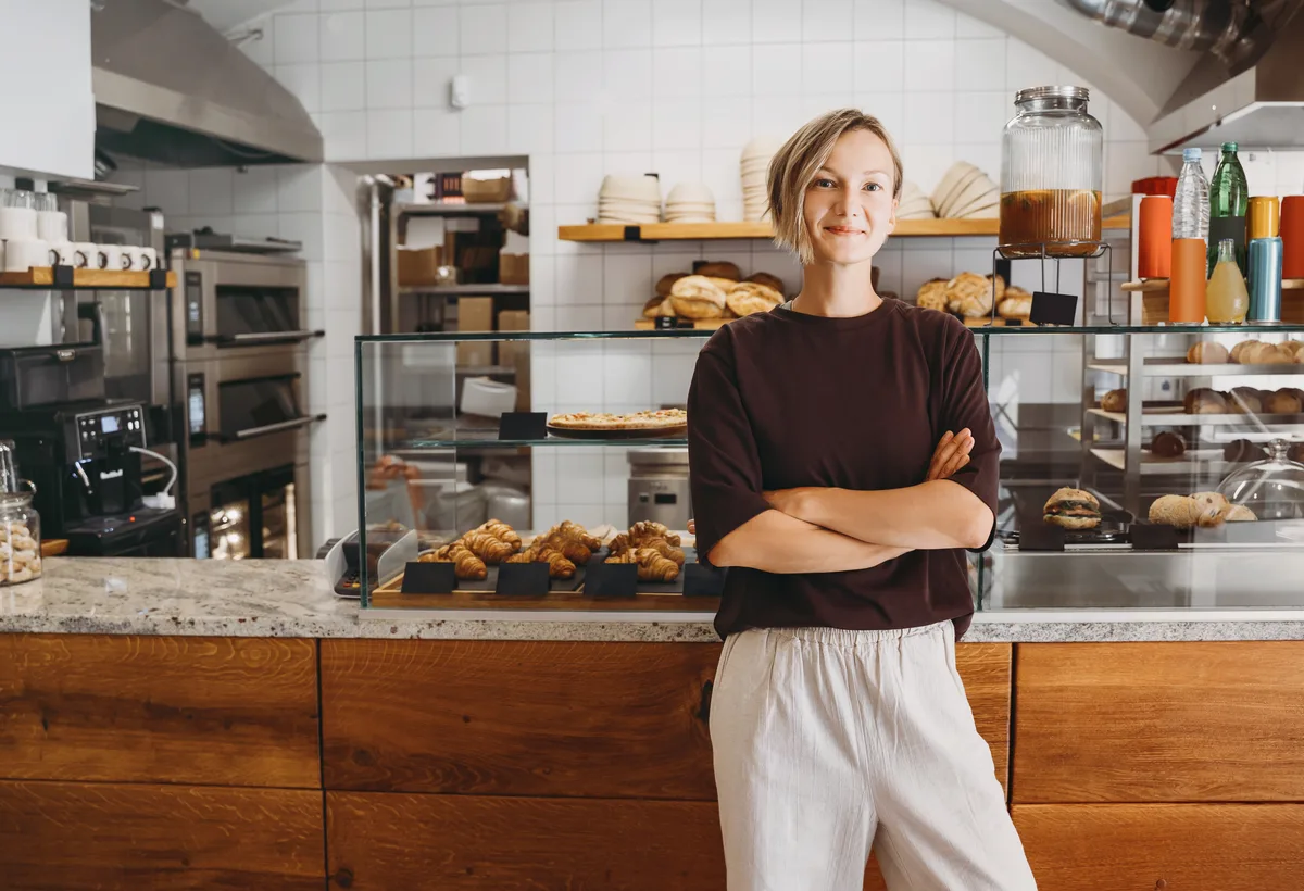A café owner standing at her counter, arms folded, ready for the day