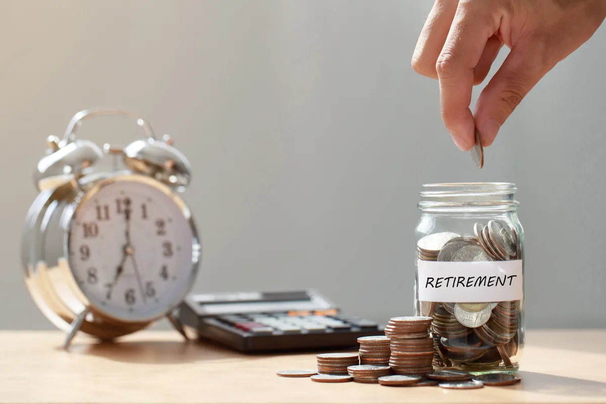 Coins dropping into a retirement savings jar beside an alarm clock