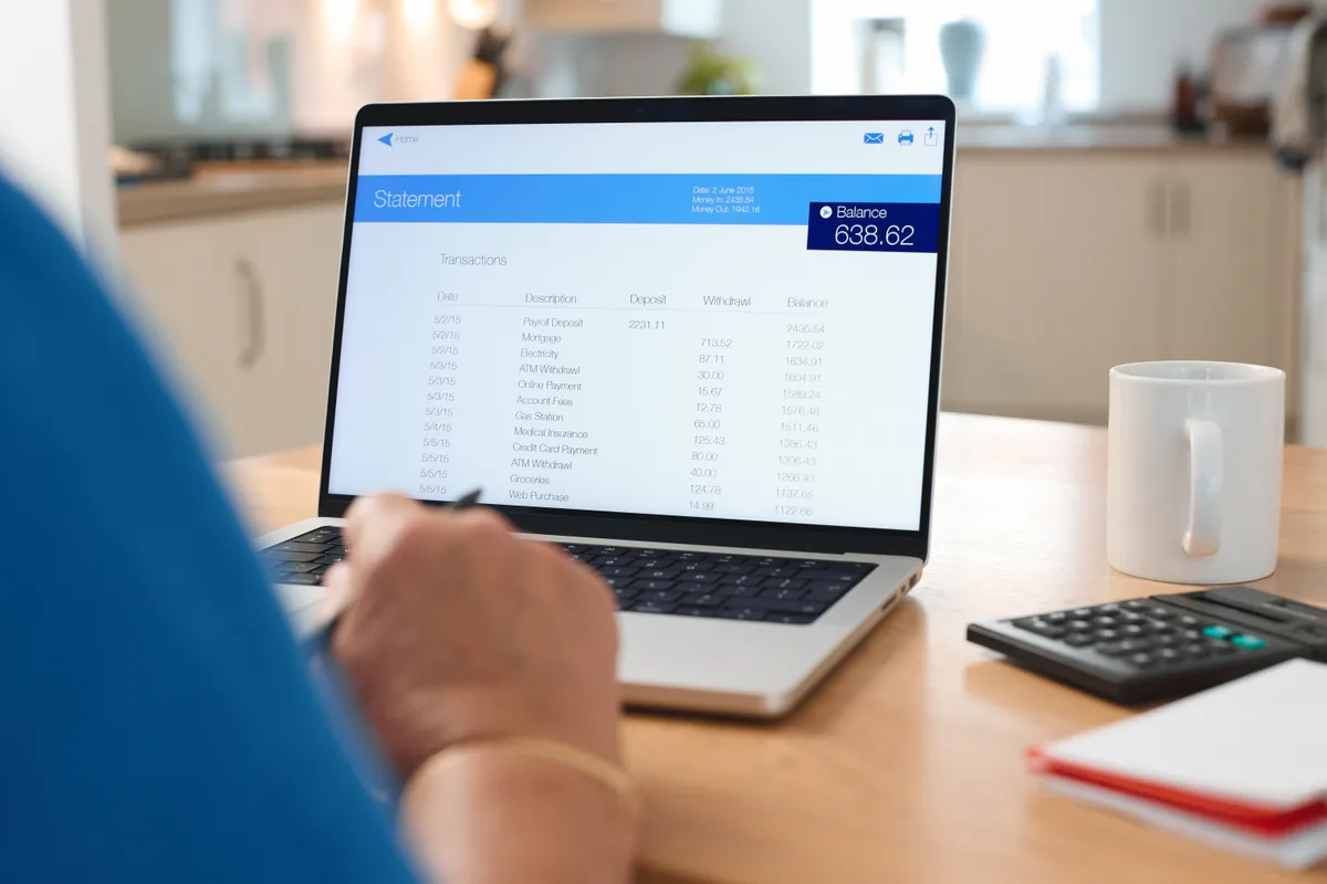 Reviewing bank statements on a laptop with a calculator alongside