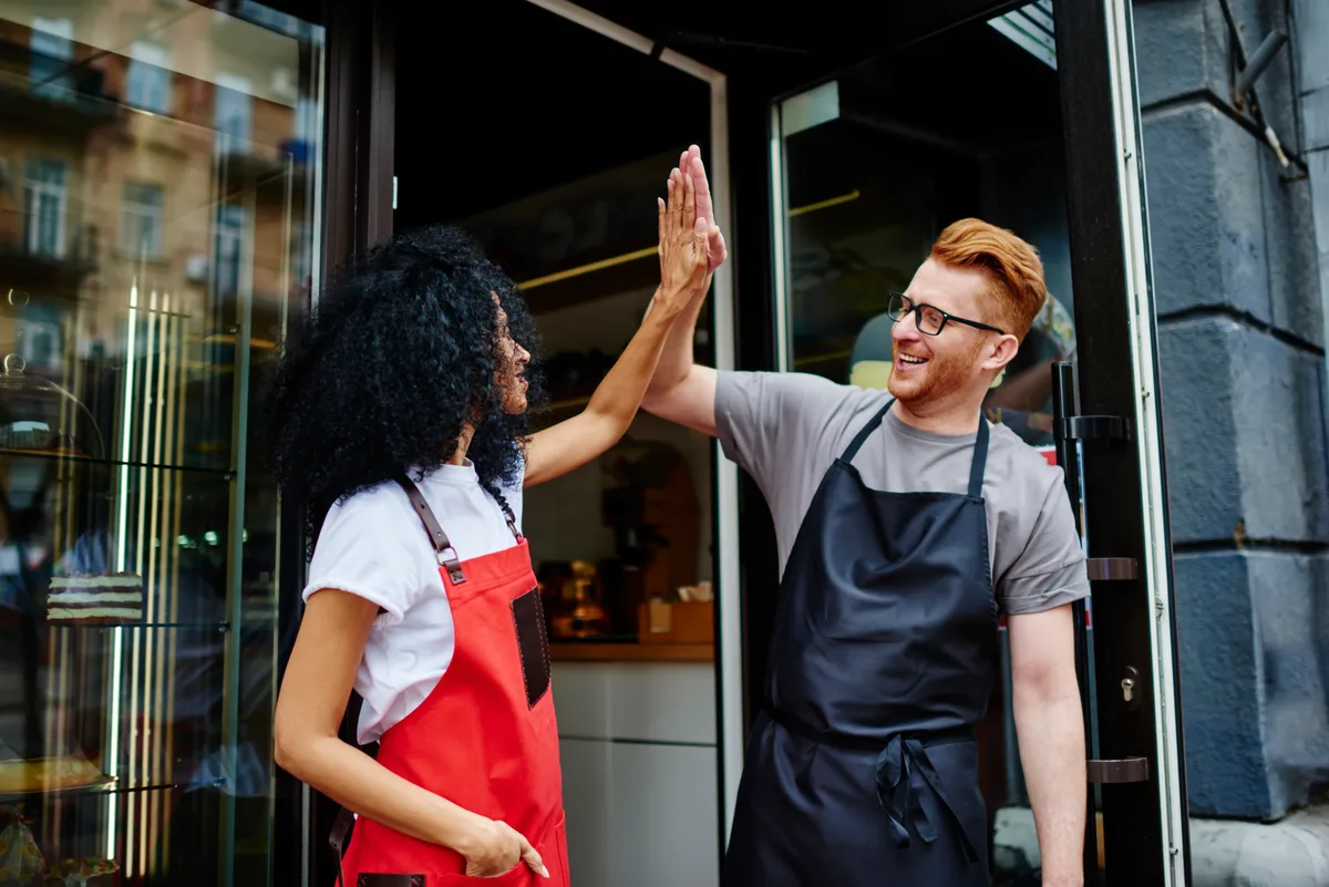 Two small business owners high-fiving at the shop door